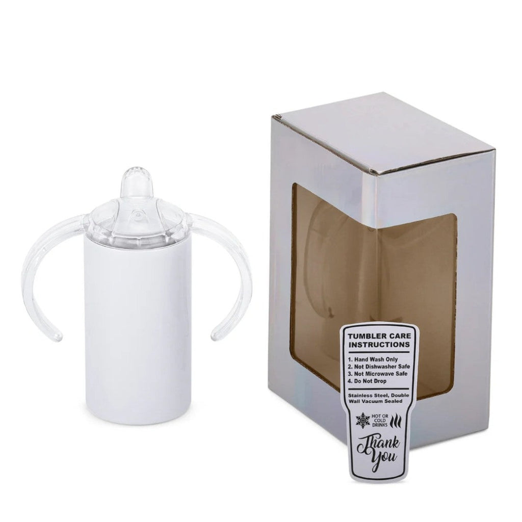 A white baby tumbler with clear silicone handles and a clear nipple top, shown next to its silver packaging box with a window and a care instructions label.