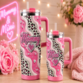 Two pink handled tumblers with a pink and black leopard print and rhinestone design, labeled 'Mommy' and 'Mini', displayed on a wooden surface with pink flowers and warm string lights in the background.