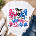 A white graphic T-shirt laid flat on a wood surface, styled with white sneakers and blue jeans. The shirt features a colorful 'Team Pink or Blue' graphic with balloons, hearts, stars, footprints, and banners reading 'What do you think? Boy or Girl?'.