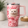A tall handled travel tumbler with a pink cherry blossom floral print and a printed white kitten in the center, shown on a marble countertop with a blurred indoor background.