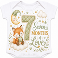 White short-sleeve baby bodysuit featuring a whimsical woodland-themed 7-month milestone graphic with a fox, crescent moon, clouds, stars, and the text 'Seven Months of Love'.