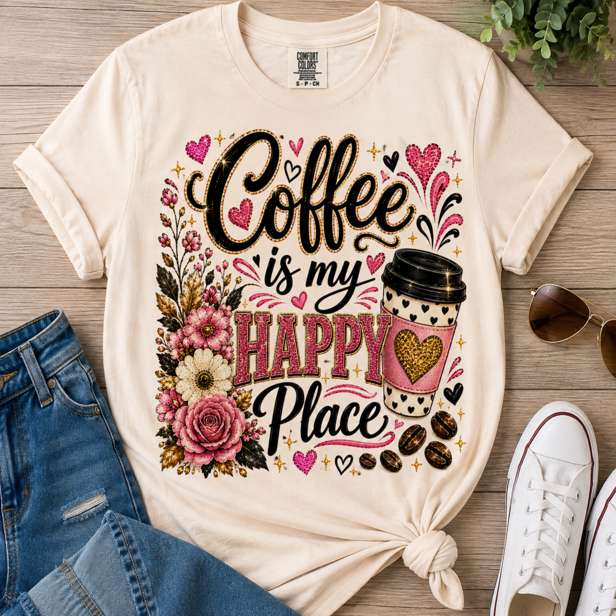 A cream-colored graphic t-shirt with a 'Coffee is my HAPPY Place' design, styled in a flat-lay arrangement with blue jeans, white sneakers, sunglasses, and a wooden background.