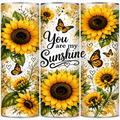 Three tall tumblers with a matching wrap design featuring bright yellow sunflowers, orange butterflies, green leaves, and the phrase 'You are my Sunshine' in black script on a cream background.