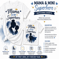 A promotional graphic for matching t-shirts showing two white shirts with printed superhero-themed designs: one reading 'Mama is my Superhero' and one reading 'Mom is my Superhero.' The layout includes watercolor-style navy silhouettes, gold stars and crown accents, descriptive text, and feature icons on a white background.