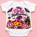 A white short-sleeve baby bodysuit laid flat on a pink background, featuring a colorful Halloween graphic with the text 'My First Halloween,' bats, a witch hat, pumpkins, flowers, a spider, and a haunted house.