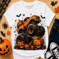 A white graphic t-shirt featuring a Halloween monster truck illustration with jack-o'-lanterns, styled in a flat-lay on a wooden surface with jeans, sneakers, and autumn props.
