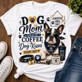 A white graphic T-shirt laid flat on a wooden surface, styled with jeans, sneakers, and a small plant. The shirt features a large dog-themed print reading 'Dog Mom Fueled by Coffee & Dog Kisses Every Day' with a French bulldog illustration, paw prints, and accessories.