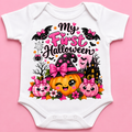 A white short-sleeve baby bodysuit laid flat on a pink background, featuring a colorful Halloween graphic with the text 'My First Halloween' and cartoon pumpkins, bats, flowers, and a witch hat.
