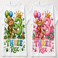 Two white short-sleeve T-shirts shown side by side, each printed with a colorful cartoon birthday design featuring a teddy bear with a dinosaur, a large number 3, balloons, flowers, and the text 'THREE Rex'.