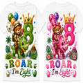 Two white short-sleeve T-shirts shown side by side, each printed with a colorful cartoon birthday design. The left shirt features a green dinosaur and brown bear with a green number 8, while the right shirt features a pink dinosaur and brown bear with a pink number 8.