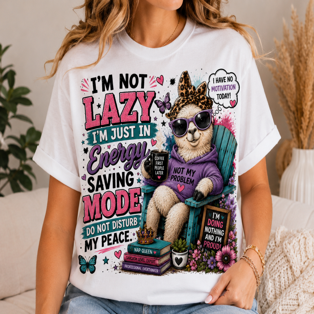 A woman wearing a white graphic t-shirt with a colorful cartoon cat sitting in a teal chair, wearing sunglasses and a leopard print hat. The text on the shirt reads 'I'M NOT LAZY I'M JUST IN Energy SAVING MODE DO NOT DISTURB MY PEACE' and other motivational phrases.