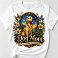 A white short-sleeve T-shirt laid flat on a light gray background, featuring a large front graphic of a golden retriever dog inside an ornate stained-glass-style frame with flowers, butterflies, and the words 'Dog Mom' and 'My Favorite Walk Starts With You.'.