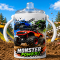 A white insulated tumbler with a clear lid and white side handles, printed with colorful monster truck graphics and the words 'MONSTER POWER!'. The tumbler is photographed outdoors on dirt with trees and a blue sky in the background.